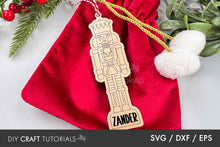 Load image into Gallery viewer, Wooden nutcracker ornament with 'Zander' on a red fabric background with Christmas decorations.