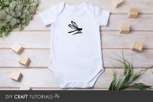 Load image into Gallery viewer, White baby onesie with a black dragonfly design on a wooden surface with flowers and blocks.
