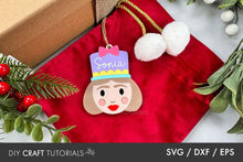 Load image into Gallery viewer, Personalized Christmas ornament with a face design and &#39;Sonia&#39; text, placed on a red fabric background with holiday decorations.
